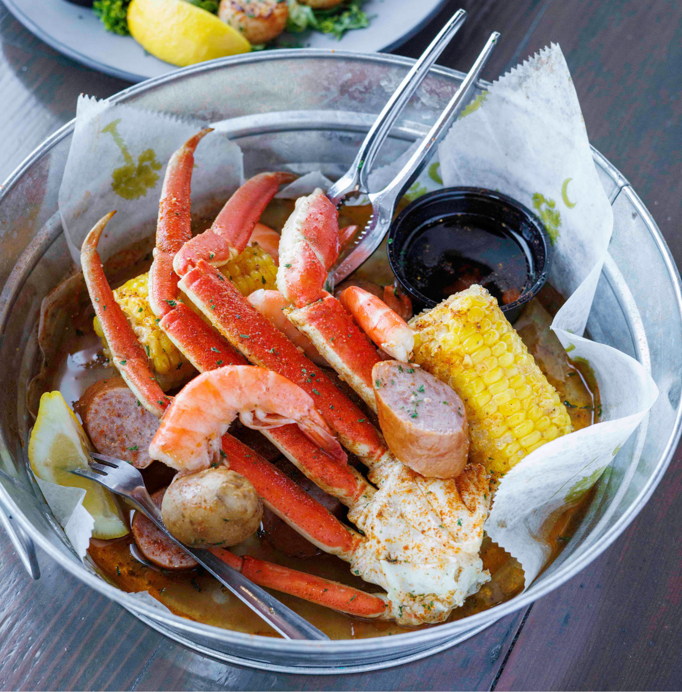 Seafood boil with crab legs, corn, and sausage in a pot on a table.